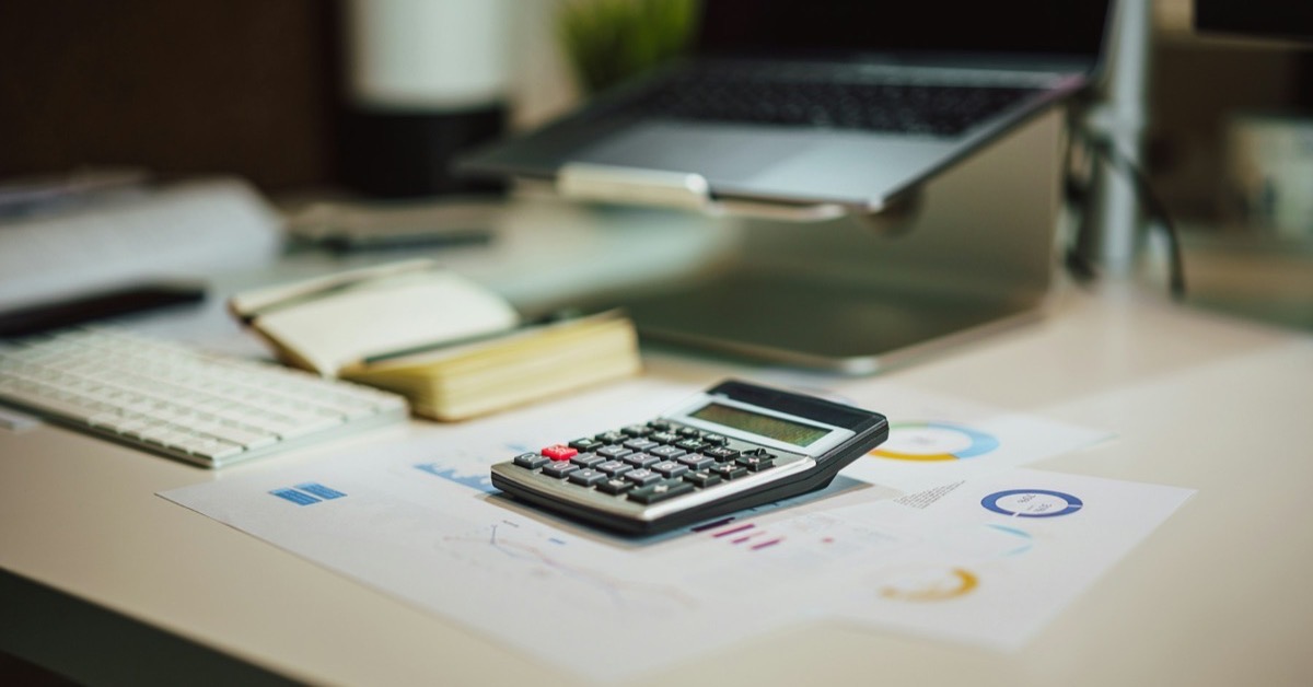 Calculatrice et graphiques de budget posés sur un bureau, à côté d'un ordinateur portable